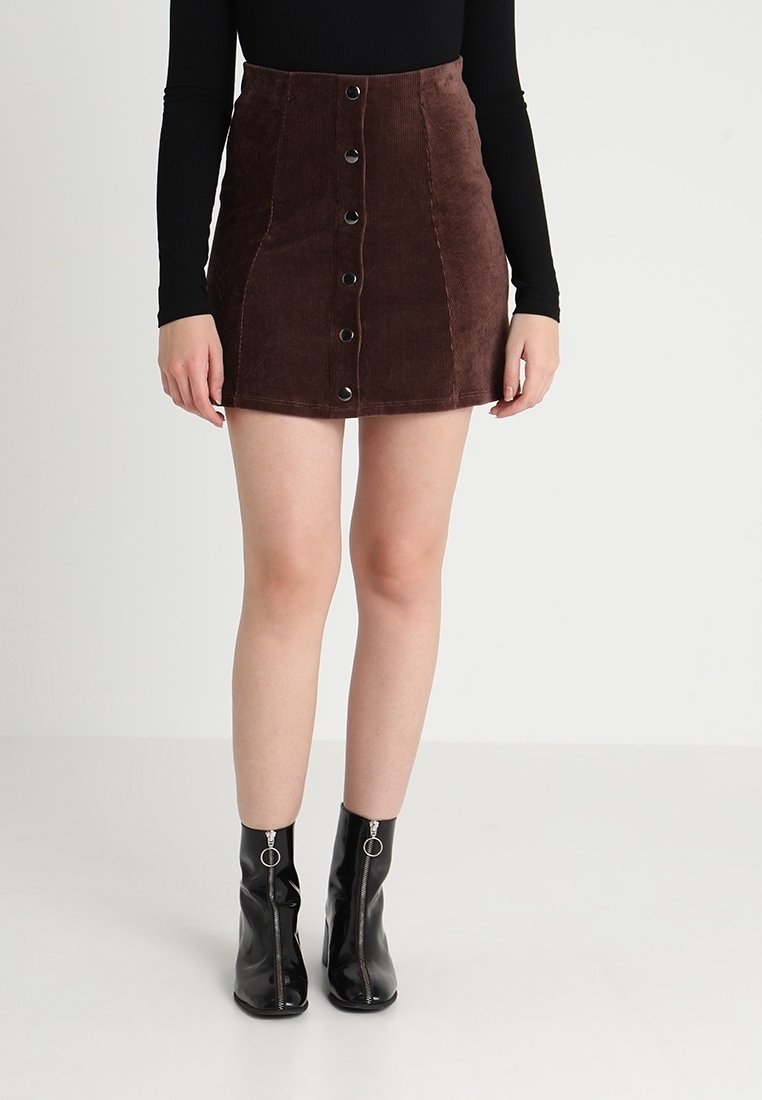 Falda mini de pana marrón con botones en la parte delantera y un corte ajustado, combinada con botas negras hasta el tobillo y una camiseta de manga larga.