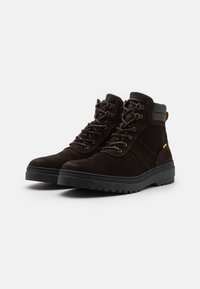Brown suede ankle boots with black rubber soles, metal eyelets, and a yellow accent. Features a padded collar for comfort.