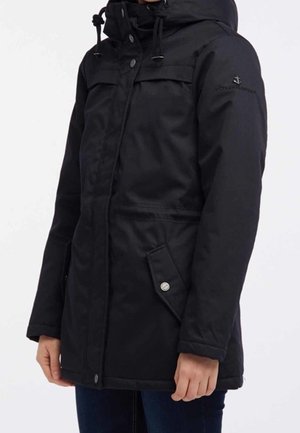 Personne portant un manteau d'hiver noir à capuche avec des poches avant à boutons et des cordons de serrage réglables sur la capuche.