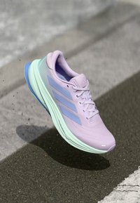 Lichtpaarse hardloopschoen met een ademende mesh bovenkant, teal accenten en drie blauwe strepen aan de zijkant. Afgeronde zool voor demping.