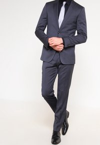Abito grigio scuro con vestibilità su misura, dotato di giacca a un bottone, colletto a punta e pantaloni slim-fit, abbinato a una cravatta grigia chiara.