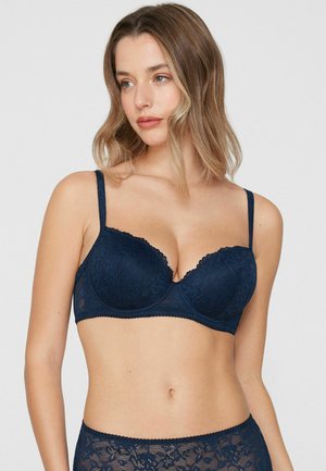 Soutien-gorge en dentelle bleu marine avec bords festonnés, armatures et bretelles réglables. Le tissu présente un motif floral avec une texture douce.