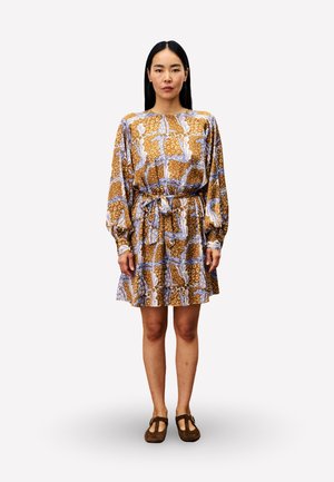 Geprinte jurk met lange mouwen, bruine, blauwe en witte bloemenmotieven, getailleerde taille, uitlopende rok, gecombineerd met bruine platte schoenen.