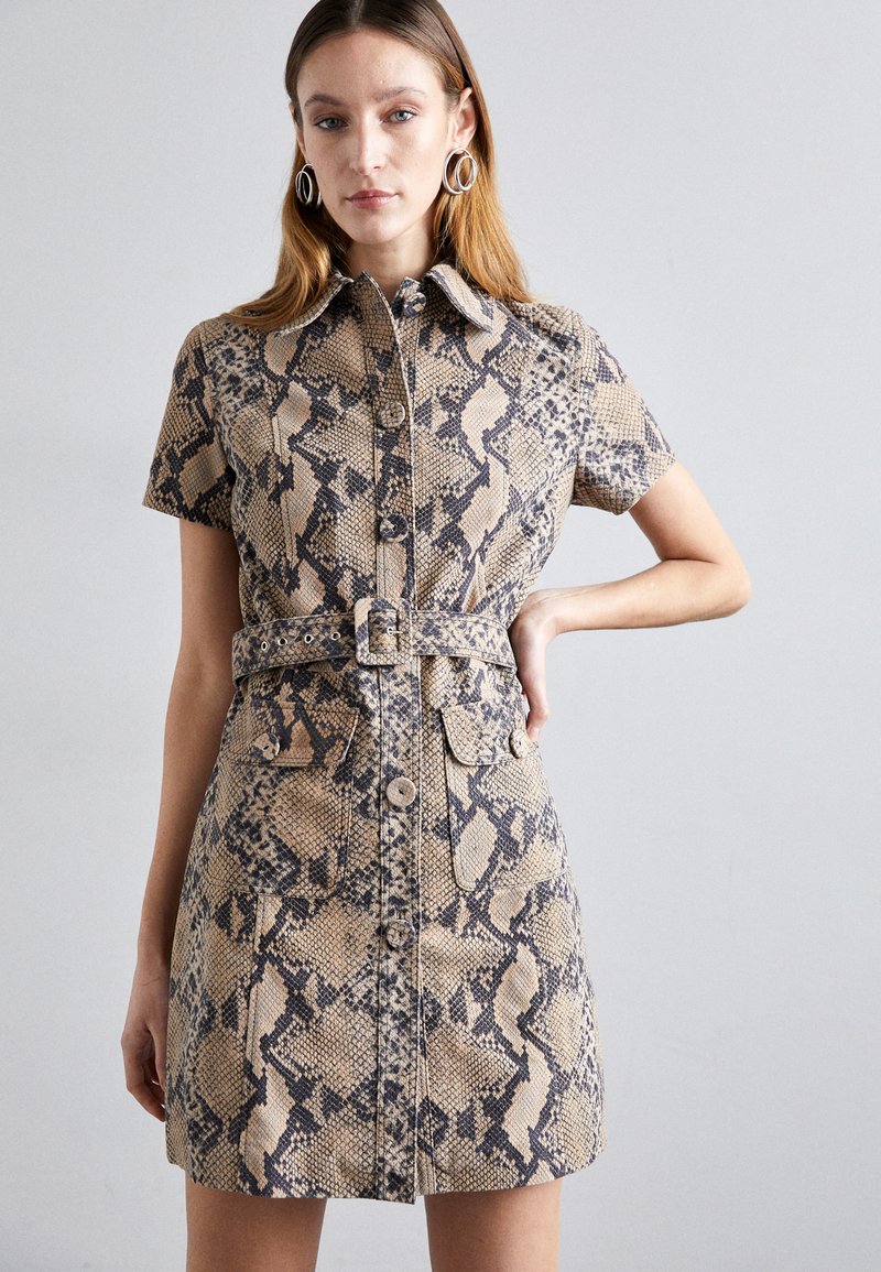 Robe chemise à manches courtes en tissu imprimé serpent, beige avec des motifs foncés, dotée d'une taille ceinturée, d'une fermeture à boutons et de deux poches avant plates.