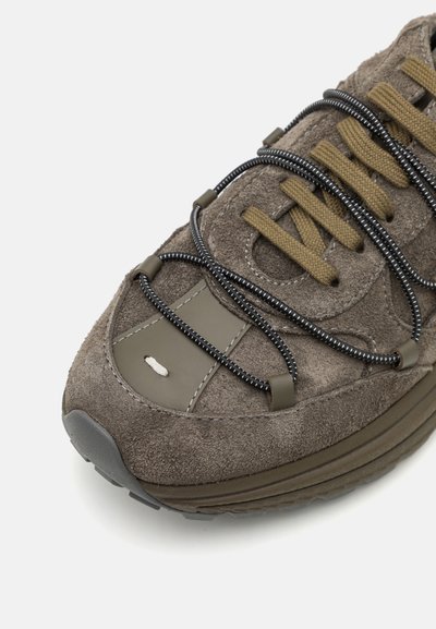 Baskets en suède grises avec semelle en caoutchouc gris foncé. Présente une surface texturée, des lacets noirs et marron, ainsi qu'un bout rond avec une accent en cuir.