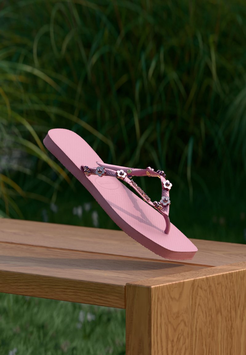 Ροζ σαγιονάρα με λουλουδάτες διακοσμήσεις που ισορροπεί στην άκρη ενός ξύλινου τραπεζιού σε εξωτερικό χώρο με πράσινα φυτά θολά στο φόντο.