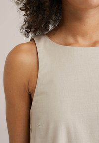 Top fără mâneci de culoare bej deschis, realizat dintr-un material texturat, cu un decolteu rotund și linii curate, evidențiind o croială lejeră și un design minimal.