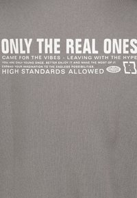 Gray t-shirt with white printed text. Text features phrases about youth and enjoyment, with an exclusive logo on the side. Smooth texture.