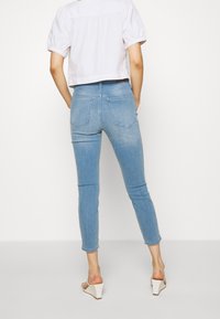 Vaqueros ajustados de color azul claro con una cintura de altura media, cuatro bolsillos y un acabado desgastado, combinados con una blusa corta blanca y tacones de cuña beige.