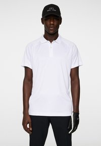 White polo shirt with a classic collar, featuring short sleeves and a smooth texture, paired with a black cap and gloves with a logo.