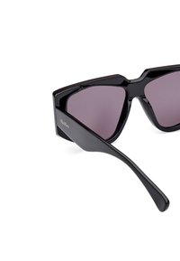 Black sunglasses with a geometric design, tinted lenses, high-shine plastic frame, and straight arms. Features logo on the side.