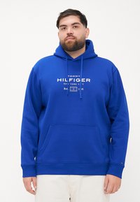 Blauwe hoodie met trekkoorden en een voork pocket. Bevat een wit tekstlogo, zachte stof en geribde manchetten. Strak, minimalistisch ontwerp.