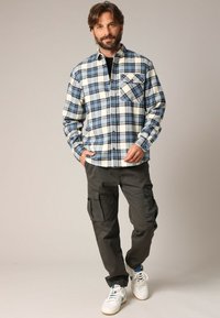 Geverfde flanellen overhemd in blauw en wit met een borstzak, gecombineerd met donkere cargobroeken en witte sneakers met blauwe accenten.