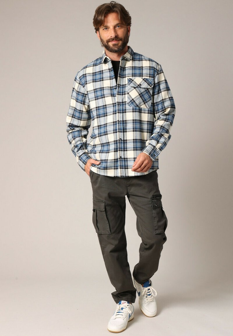 Geverfde flanellen overhemd in blauw en wit met een borstzak, gecombineerd met donkere cargobroeken en witte sneakers met blauwe accenten.