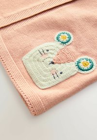 Gebreide deken in zachtroze met een gestructureerd oppervlak. Heeft een witte berenkop applicatie met kleurrijke ronde oren en geborduurde details.
