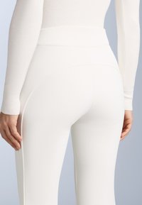 Colanți albi cu talie înaltă, dintr-un material elastic, cu o textură netedă și o formă ajustată, având un design fără cusături și detalii de cusătură subtile.