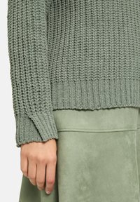 Hellgrüner gestrickter Pullover mit einem strukturierten Muster, mit gerippten Bündchen und Saum, kombiniert mit einem glatten, gleichfarbigen Rock.