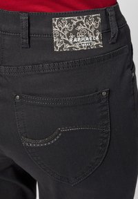 Pantaloni in denim nero con etichetta floreale. La tasca posteriore presenta cuciture a contrasto e un piccolo rivetto metallico è visibile sul lato.