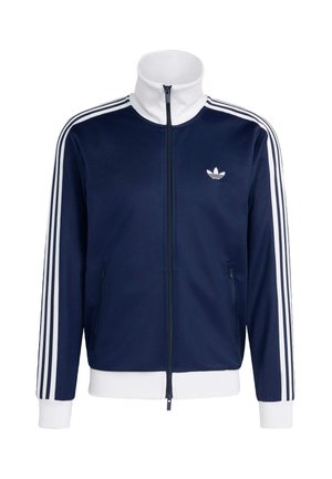 Μπουφάν αθλητικό σε ναυτικό μπλε με λευκό φερμουάρ, ψηλό γιακά και λογότυπο. Διαθέτει λευκές ρίγες κατά μήκος των μανικιών και ριμπ μανσέτες και τελείωμα.