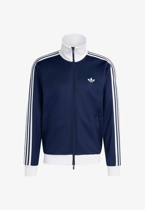 Námořnicky modrá sportovní bunda na zip s bílým zipem, vysokým límcem a logem. Má bílé pruhy podél rukávů a žebrované manžety a lem.