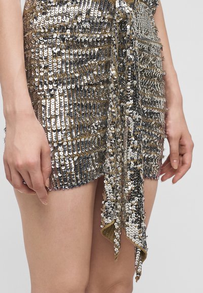 Gros plan d'une personne portant une jupe courte recouverte de sequins argentés et dorés densément placés avec un détail noué à l'avant.