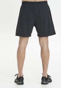 Svarta idrottsshorts med elastisk midja, slät textur, knä-lång skärning och minimalistisk design. Bärs med svarta löparskor.