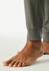 Grijze katoenen joggingbroek met elastische boorden, gecombineerd met een blote voet die opvallende tenen en de kromming van de voet toont. Gladde textuur.