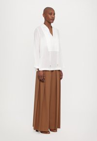 Blusa bianca leggera con colletto e scollo a V, abbinata a una lunga gonna marrone fino al pavimento con pince.