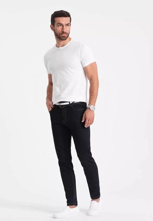 Bílý tričko s kulatým výstřihem spárované s černými skinny džínami se žlutým prošíváním. Nosí se s bílými slip-on botami a stříbrnými hodinkami.