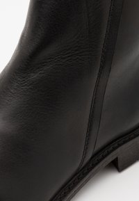 Bota de cuero negra que presenta una textura suave, detalles de costura vertical y un tacón negro resistente. Enfoque en la artesanía y la calidad del material.