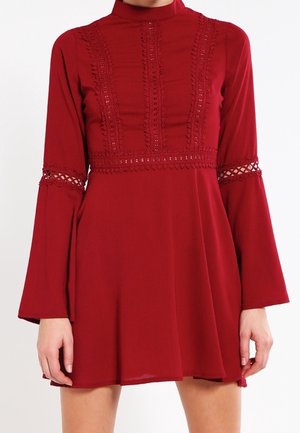 Robe rouge à manches longues avec des détails en dentelle sur la poitrine et les manches, jupe évasée et col montant.
