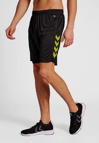 Shorts de sport noirs en matériau léger, avec un motif chevron vert sur le côté, dotés d'une ceinture élastique.