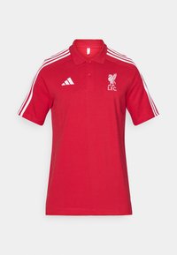 Punainen polo-paita, jossa on valkoinen Adidas-logo oikeassa rinnassa, Liverpool FC -embleemi vasemmassa rinnassa ja kolme valkoista raitaa kummallakin olkapäällä.