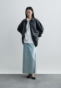 Black leather overshirt with front pockets, layered over a white shirt, paired with a light blue denim skirt featuring a side slit and black flats.