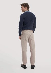 Marineblauwe trui, lichtblauwe kraag en lichtbeige jeans met een rechte snit. Donkere schoenen, minimalistisch ontwerp, gladde stof en geen zichtbare patronen.