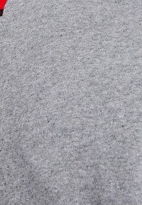 Tejido de algodón gris con una textura suave y un ligero patrón jaspeado. Presenta un ribete rojo en el cuello. Adecuado para un estilo informal.