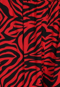 Rode stof met gedurfde zwarte zebra-stripes, met een soepele textuur en een geraffineerde taille. Geschikt voor een casual of speelse outfit.