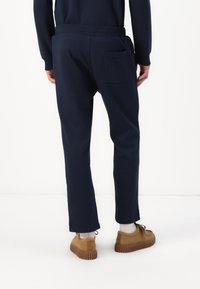 Navyblauwe sweatpants met een drawstring tailleband en een enkele achterzak, gemaakt van zachte stof. Gecombineerd met lichtbruine schoenen en witte sokken.