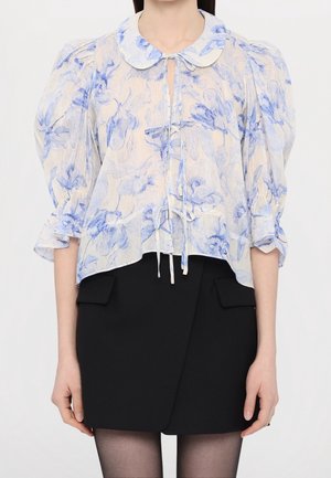 Lichte blouse met blauwe bloempatronen op een crèmekleurige achtergrond, met een spitse kraag en een strik bij de hals. Poefmouwen.