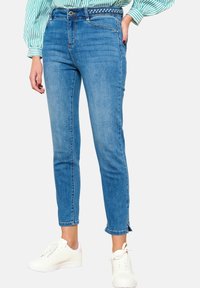 Vaaleansiniset farkut, joissa on istuva malli, keski-vyötärö, punottu vyö ja nilkkapituiset lahkeet, joissa on halkiot. Yhdistettyinä valkoisiin lenkkareihin.