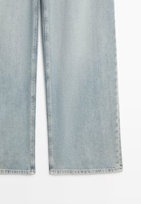 Lichtblauwe denim jeans met wijde pijpen, waarbij het onderste gedeelte en de zoomstiksel op een witte achtergrond worden getoond.