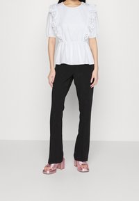 Weiße Bluse mit voluminösen Ärmeln, schwarze Hosen und metallic-pinke Blockabsatzsandalen. Glattes Material mit floralen Akzenten.