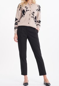 Beige kofta med svart blommönster, rund halsringning och knappar, kombinerad med svarta raka byxor och svarta ballerinaskor.