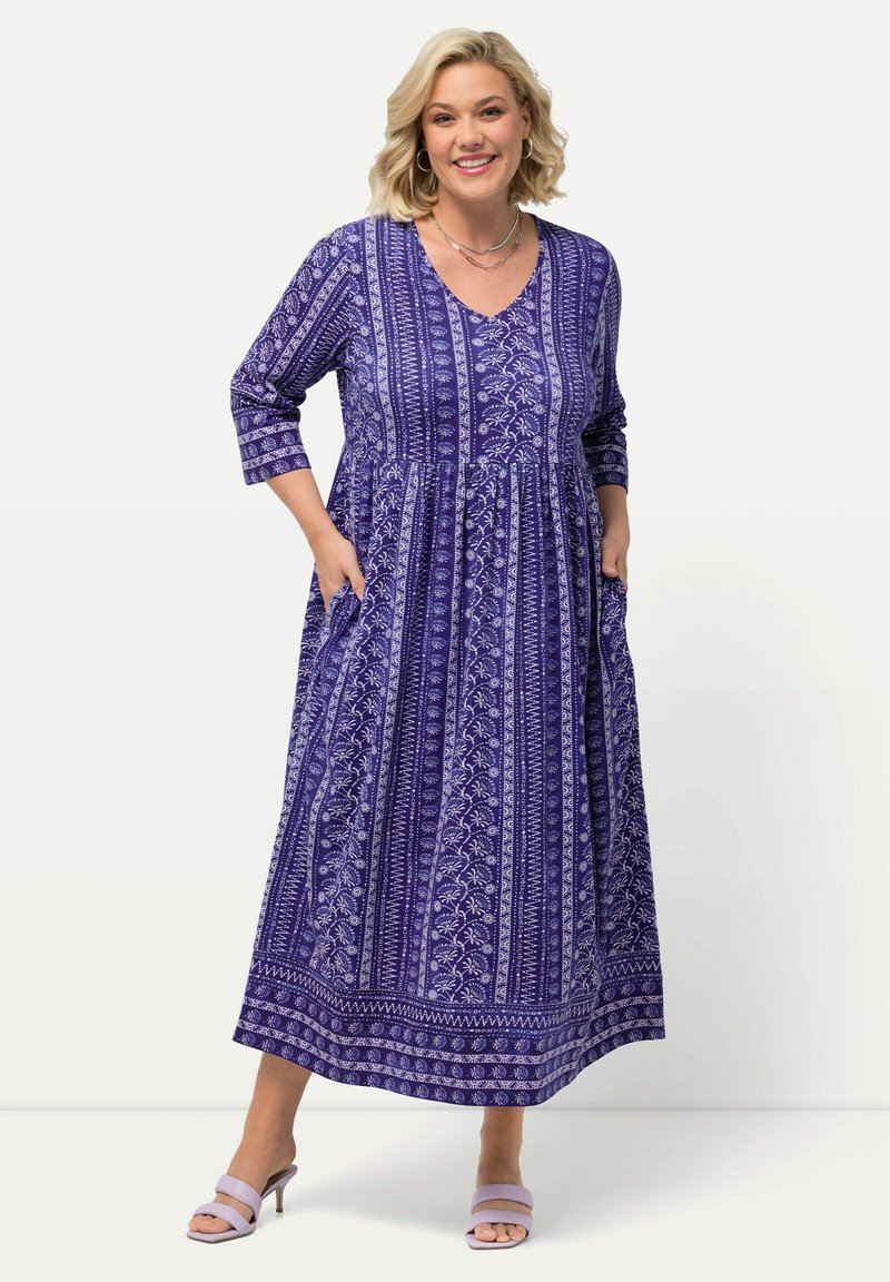 Purppurainen maksimekko, jossa on V-kareksi, kolme neljännesriceet, kukkakuviot ja taskut. Kevyt kangas ja virtaava muotoilu.