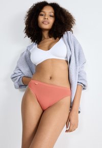 Let grå hættetrøje, hvid bh og koralfarvet trusse. Trussen har en glat struktur med et lille logomærke på siden.