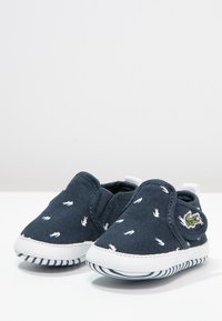 Navy slip-on boty s bílým vzorem otisků rukou, textilní svršek, elastické boční panely a bílá gumová podrážka se pruhovanými detaily.