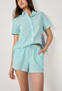 Gestreepte twee-delige set in licht teal en wit, bestaande uit een kortärmige overhemd met knopen en bijpassende shorts met trekkoord en bloemenborduursel.