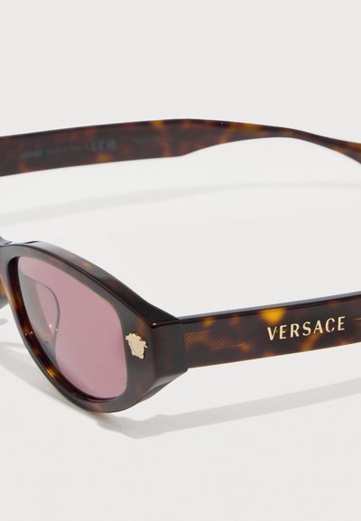 Γυαλιά ηλίου με σκελετό τύπου cat-eye από τεθλασμένο χρώμα φολιδωτού χελώνας και μοβ φακούς, με χρυσό έμβλημα Medusa και το λογότυπο "Versace" στο πλαϊνό μπράτσο.