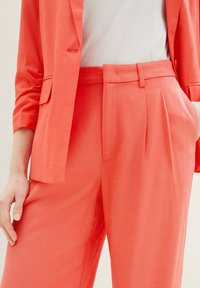 Coral blazer and matching trousers with a smooth texture. Blazer features a single lapel and pocket; pants have a pleated front design.