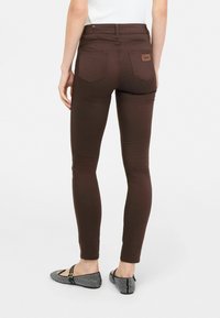 Jeans skinny marroni con vita alta, due tasche posteriori e una patch in pelle. Abbinati a ballerine con un motivo bianco e nero.